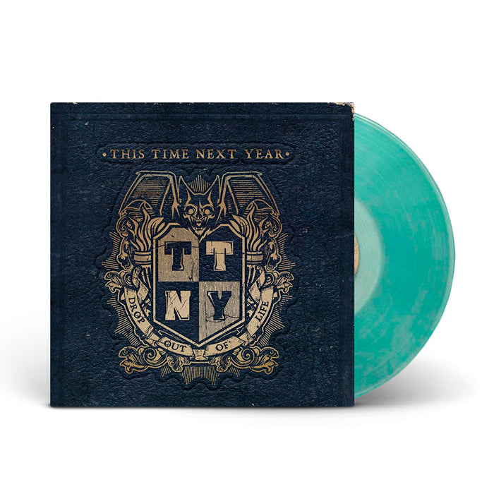 A Coke Bottle Green marbled vinyl record by This Time Next Year partially slides from a dark blue cover with a gold bat crest and the initials TTNY. The text reads “This Time Next Year” and “Drop Out Of Life.”.