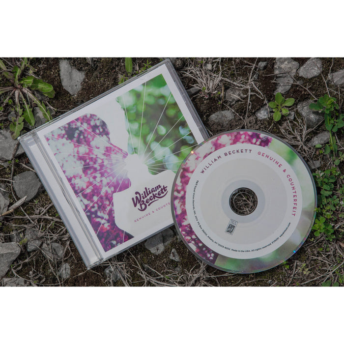 CD and CD cover photographed outside on the ground. CD is green, pink and white. CD cover has 2 figures facing each other, one is green and one is pink. There is a ray of white light between them. The bottom of the cover has "WILLIAM BECKETT" printed in dark pink font. Below that is printed "GENUINE AND COUNTERFEIT".