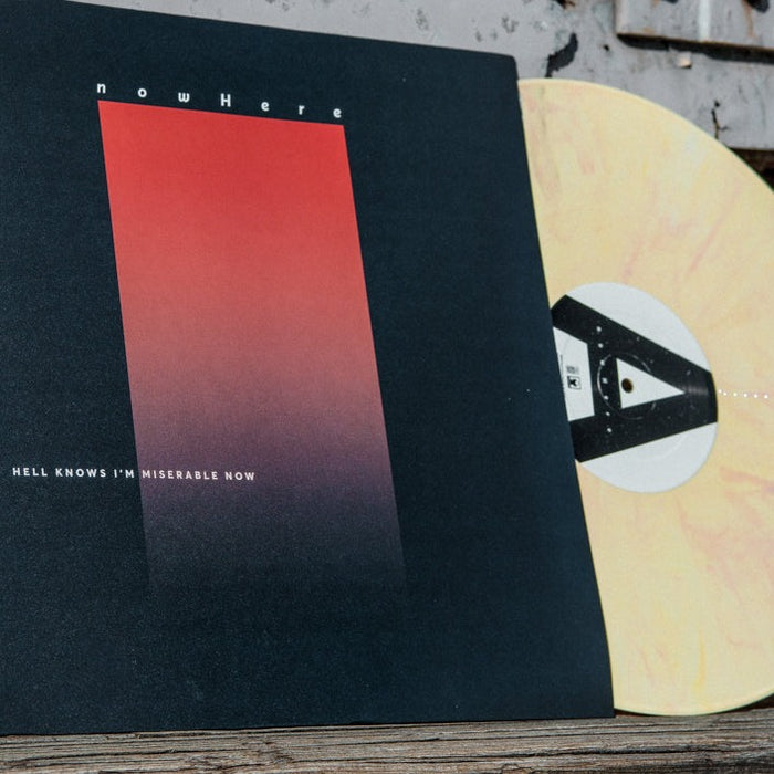 Record against white background. Vinyl is cream color with light orange swirls. Record jacket is a dark blue background with an ombre orange rectangle standing vertically in the center. The top of the rectangle has "NOWHERE" printed and the bottom left corner has "HELL KNOWS I'M MISERABLE NOW" printed. Record is placed outside leaning up against the side of a building.