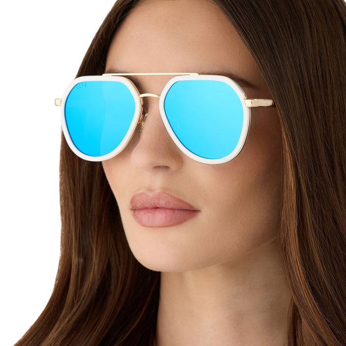 on model - female wearing diff eyewear featuring the joey round sunglasses with a snowbound & gold metal frame with blue mirror lenses detailed view