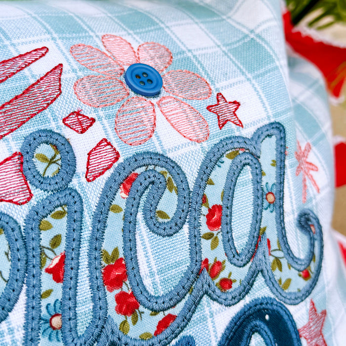 Decorative pillow with floral patterns and embroidered text on a floral background