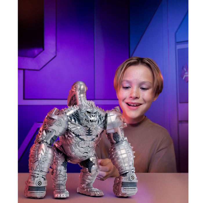 A smiling young boy stands behind a large silver monster toy on a table, with a purple-lit futuristic room in the background.
