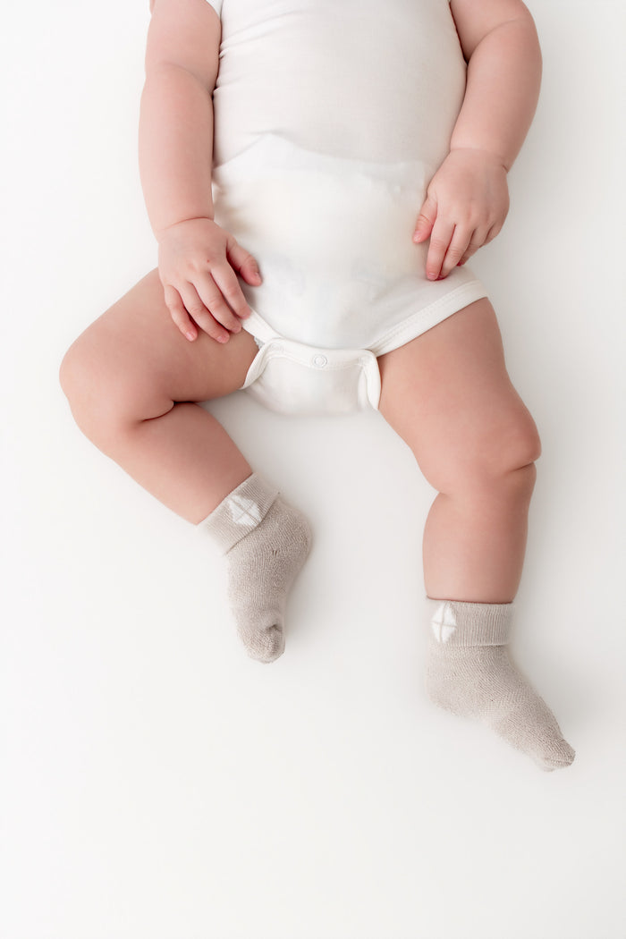 A baby lying on a white surface wearing a white bodysuit and light gray socks.