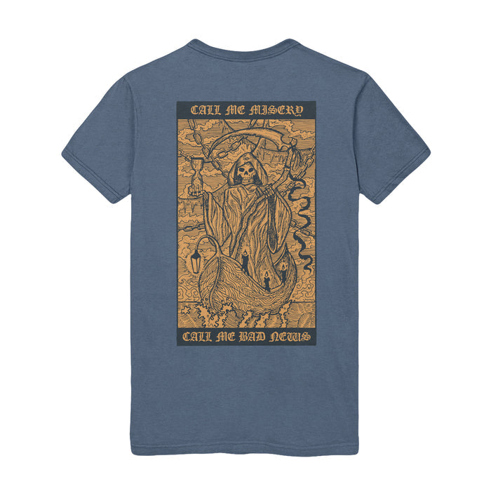 Back of Blue Jean colored short sleeve shirt with rectangle across the back. Inside the rectangle is a creature similar to the grim reaper riding in a wooden boat on the water. On top of that, there is text that says CALL ME MISERY. On the bottom of the image, there is text that says CALL ME BAD NEWS.