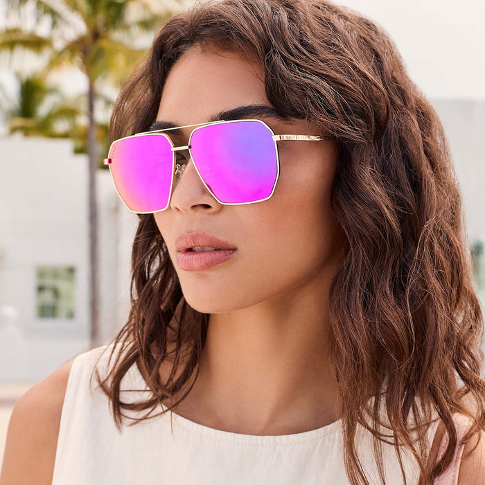 lifestyle - female outdoors wearing diff eyewear featuring the berkely navigator sunglasses with a gold frame and pink rush mirror lenses angled view