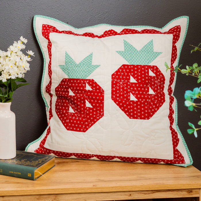 Decorative pillow with red and green patterns on a wooden surface with a dark background
