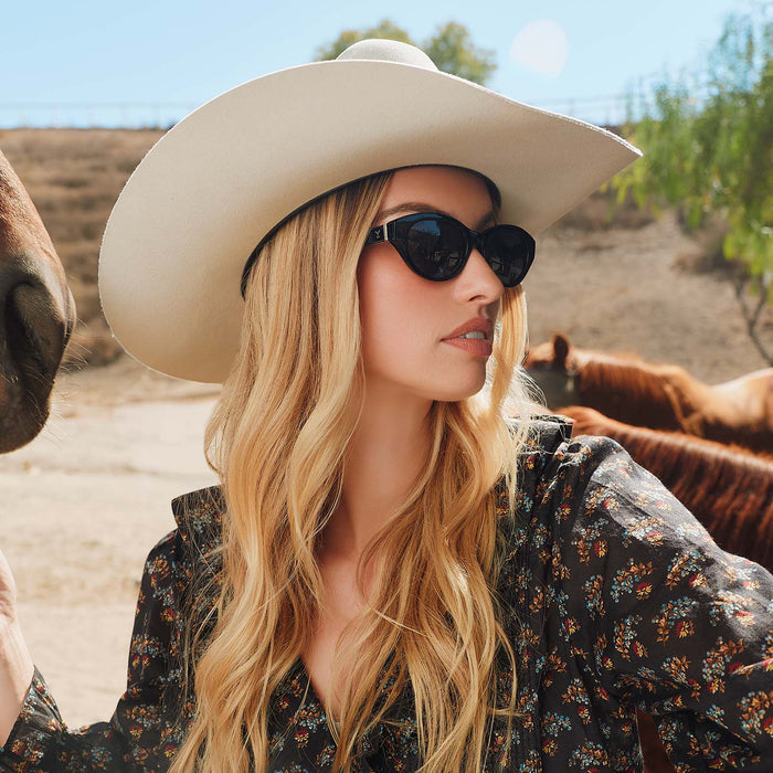 lifestyle - blonde female in the desert wearing yellowstone x diff eyewear featuring the teeter round sunglasses with a classic black acetate frame and grey polarized lenses angled view