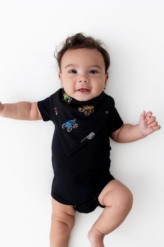 Baby wearing black Bib in Monster Truck print over a black bodysuit on white background