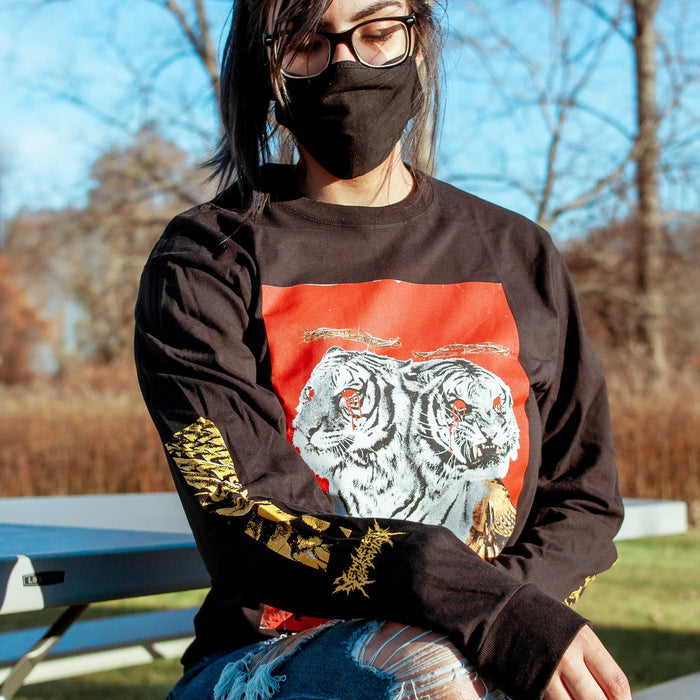 Someone wearing the Long sleeve shirt that has an image with a red background and a two headed white tiger with gold wings on the front of the vinyl cover. There are also red roses at the bottom of the cover, blood coming from both tiger’s eyes, and a crown of thorns above both of the tigers heads. On the sleves which contain gold lettering for the band POLYPHIA