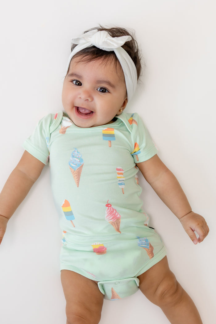 Baby smiling in a Mint Ice cream print Bodysuit with a white Bow headband on a beige background