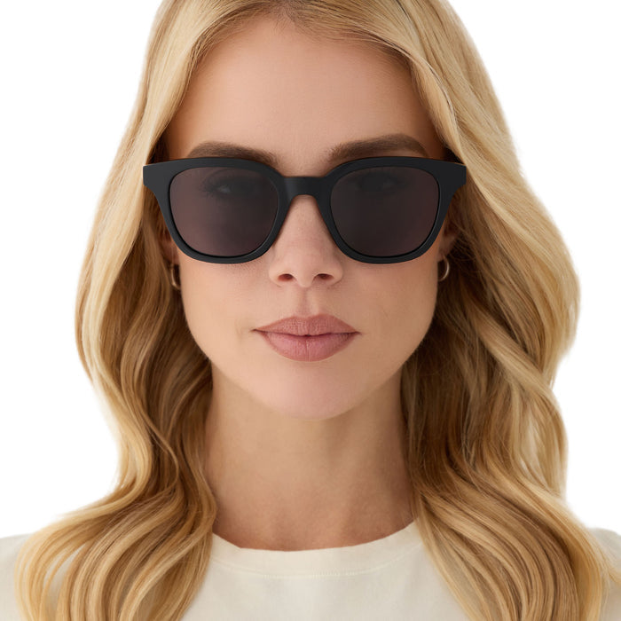 on model - female wearing diff eyewear featuring the bridget round sunglasses with a black with gold frame and grey polarized lenses front view