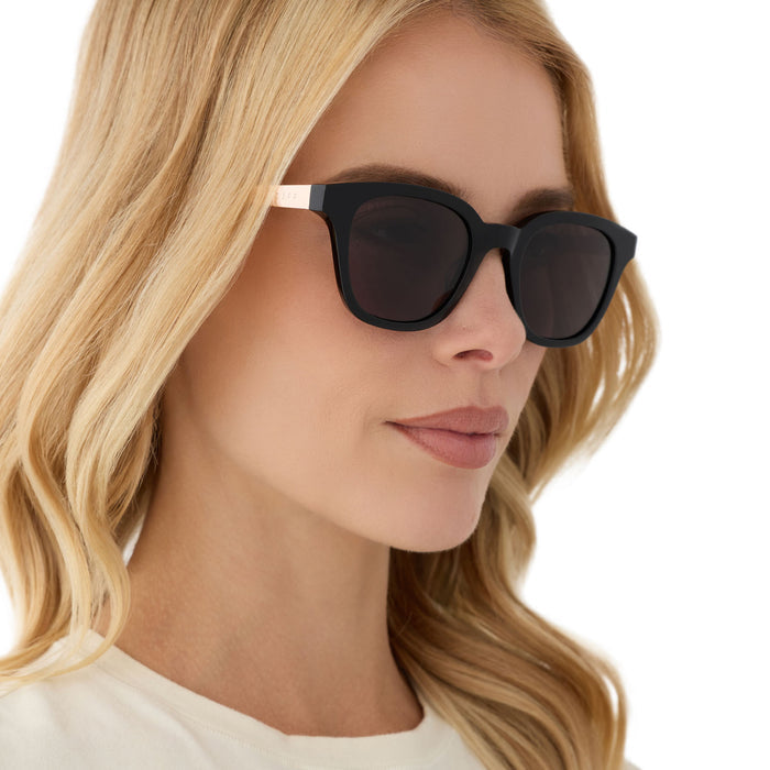 on model - female wearing diff eyewear featuring the bridget round sunglasses with a black with gold frame and grey polarized lenses angled view
