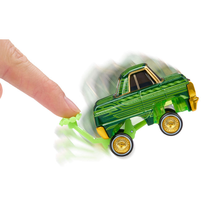 Green toy car with gold wheel rims being pushed by a finger on a white background