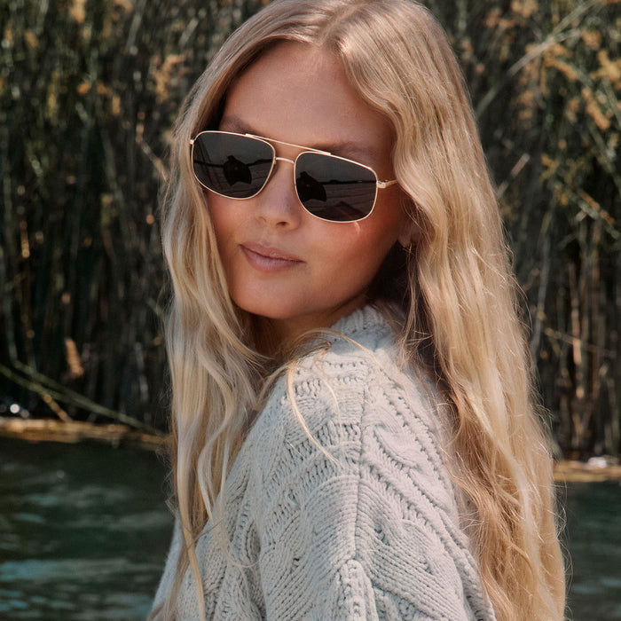 lifestyle - blonde female wearing diff eyewear featuring the charley navigator sunglasses with a gold metal frame and brown polarized lenses front view
