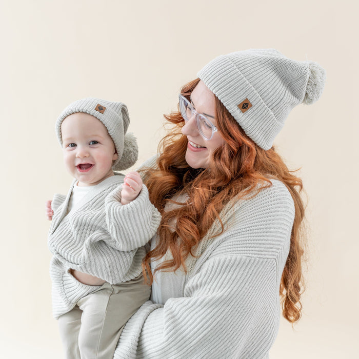 Mom and child wearing matching Kyte Baby Chunky Knit Pom Beanies in Oat