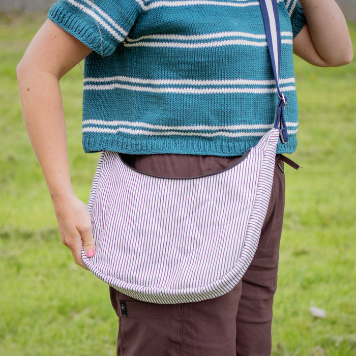Person wearing a blue striped sweater and holding a white bag with black stripes in a grassy field.