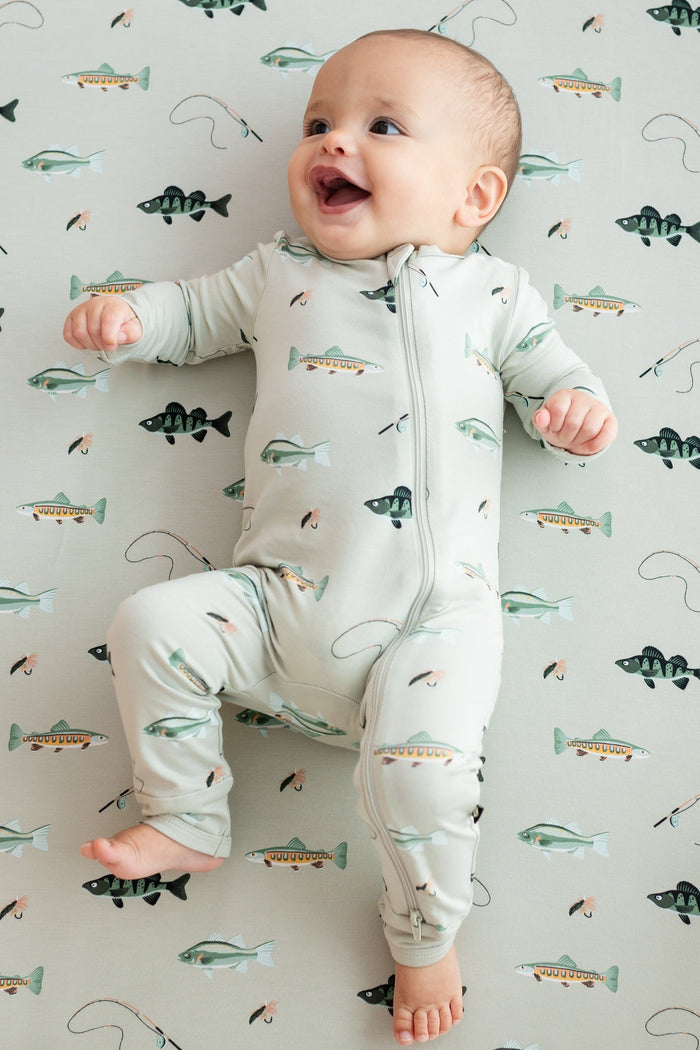 Smiling infant laying on a Fishing crib sheet wearing the Zippered Romper in Fishing