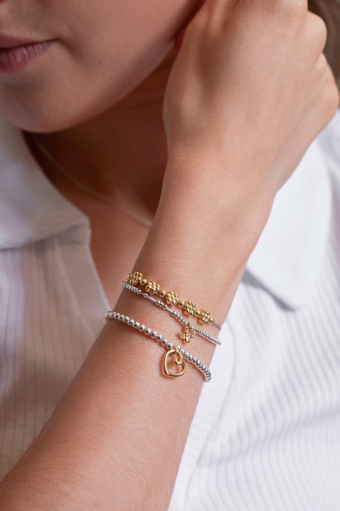 Close-up of a person's wrist wearing multiple gold and silver bracelets on a white background