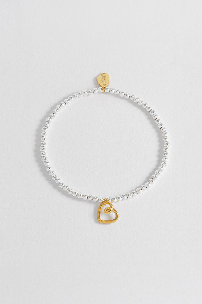 Silver bracelet with a gold heart charm on a light gray background