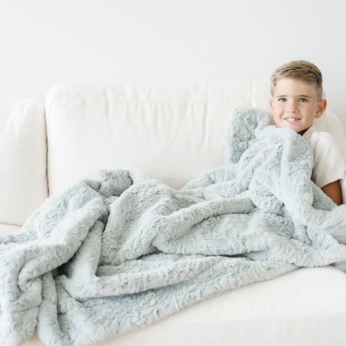 Boy snuggled on couch with a mint green dream faux fur soft toddler blanket.