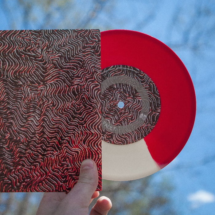 Record and jacket photographed outside with trees in the background. Vinyl is white and red split through the center. Jacket is a picture of black and red squiggly lines going different directions. Individual is holding record and jacket in their hand.