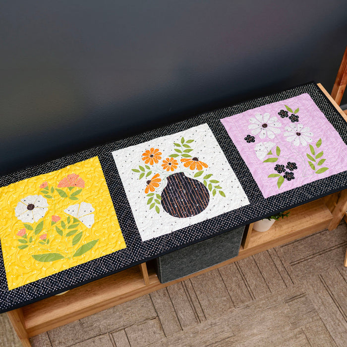 Three floral quilted placemats on a wooden table against a dark background
