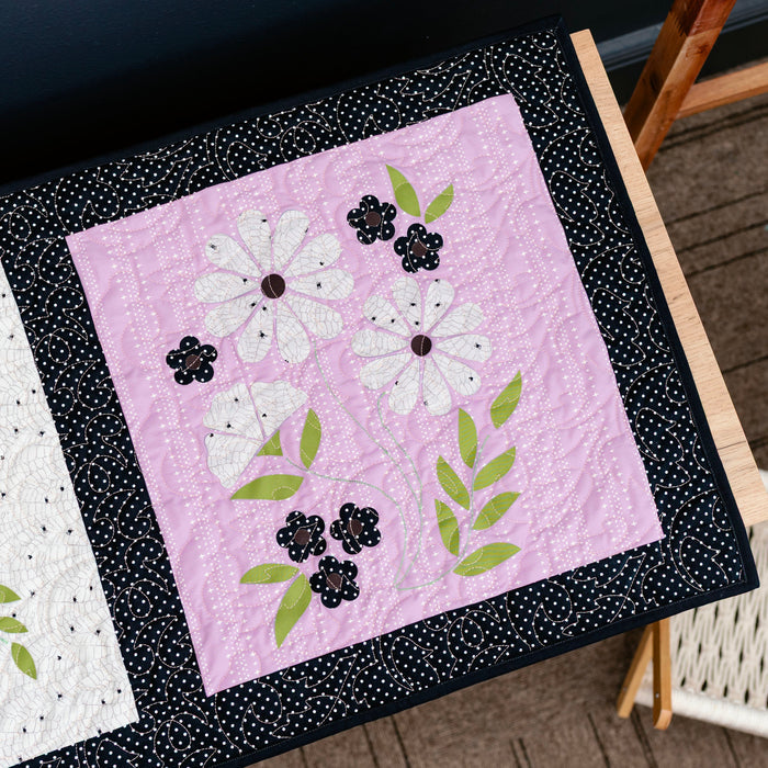 Two quilted blocks with floral designs on a wooden surface.