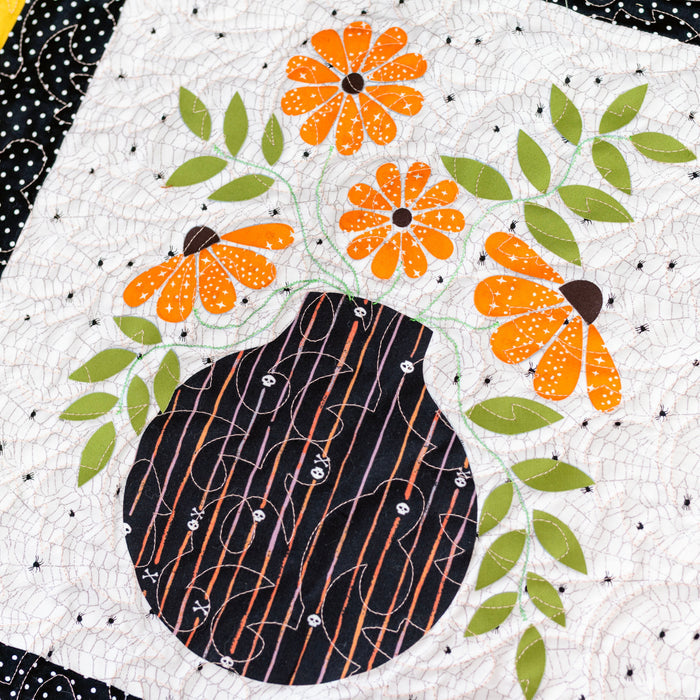 Quilt block with a black vase and orange flowers on a white background