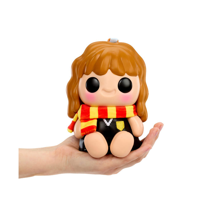 Toy figure of a girl character with brown hair and a red and yellow scarf held in a hand on a white background