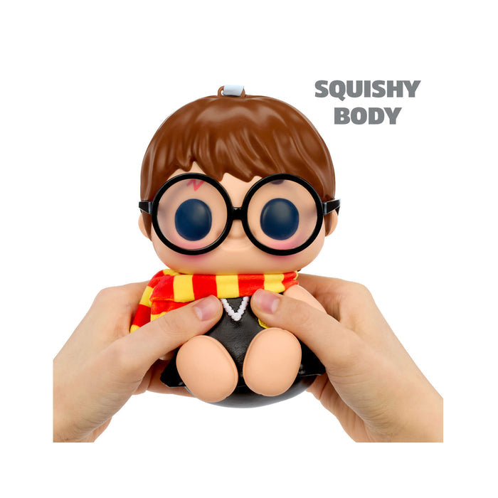 Toy figure of a character with glasses and a scarf, held by hands on a white background.