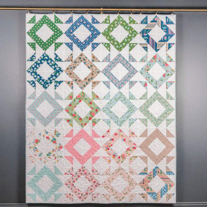 Colorful quilt with geometric patterns hanging on a gray wall.