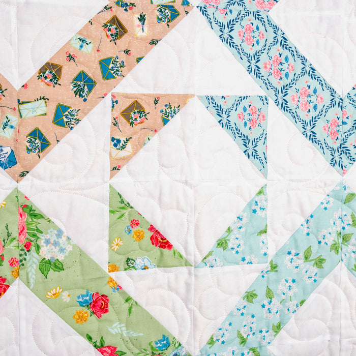Quilt with diamond pattern featuring various floral fabrics on a white background