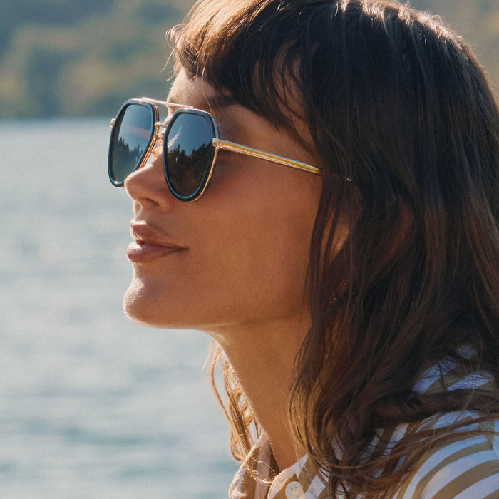 lifestyle - female at the lake wearing diff eyewear featuring the joey round sunglasses with a black & gold metal frame with grey gradient polarized lenses side view