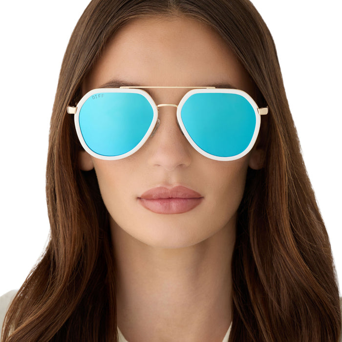 on model - female wearing diff eyewear featuring the joey round sunglasses with a snowbound & gold metal frame with blue mirror lenses front view