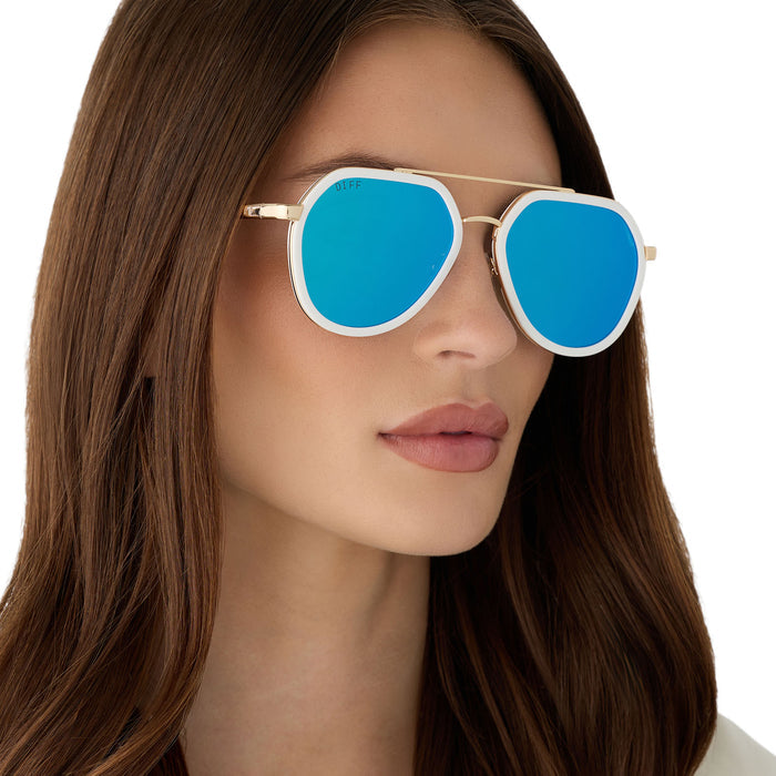 on model - female wearing diff eyewear featuring the joey round sunglasses with a snowbound & gold metal frame with blue mirror lenses angled view