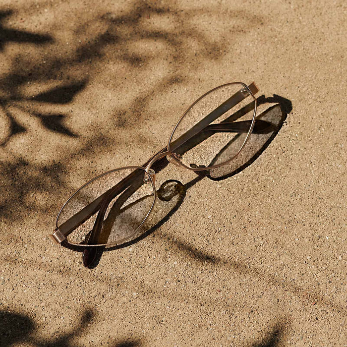 still life - jojo fletcher x diff eyewear jordy cat eye prescription glasses with a gold metal frame chocolate crystal temples laying on sand