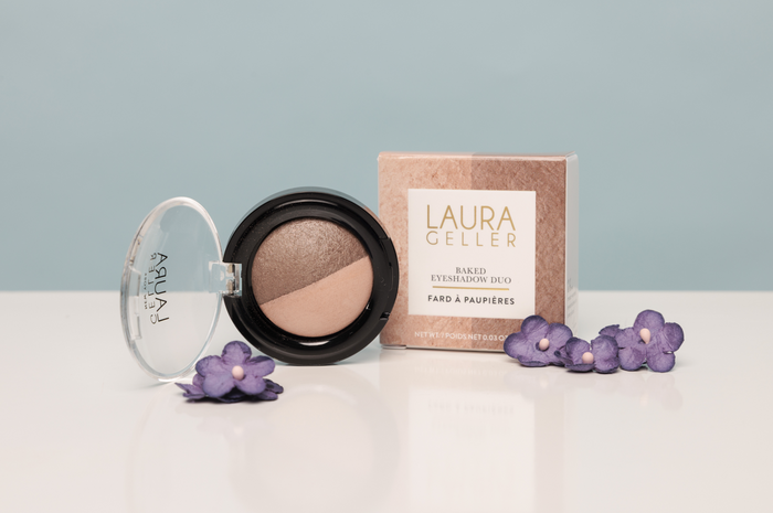 Laura Geller makeup product with packaging on a light surface with flowers