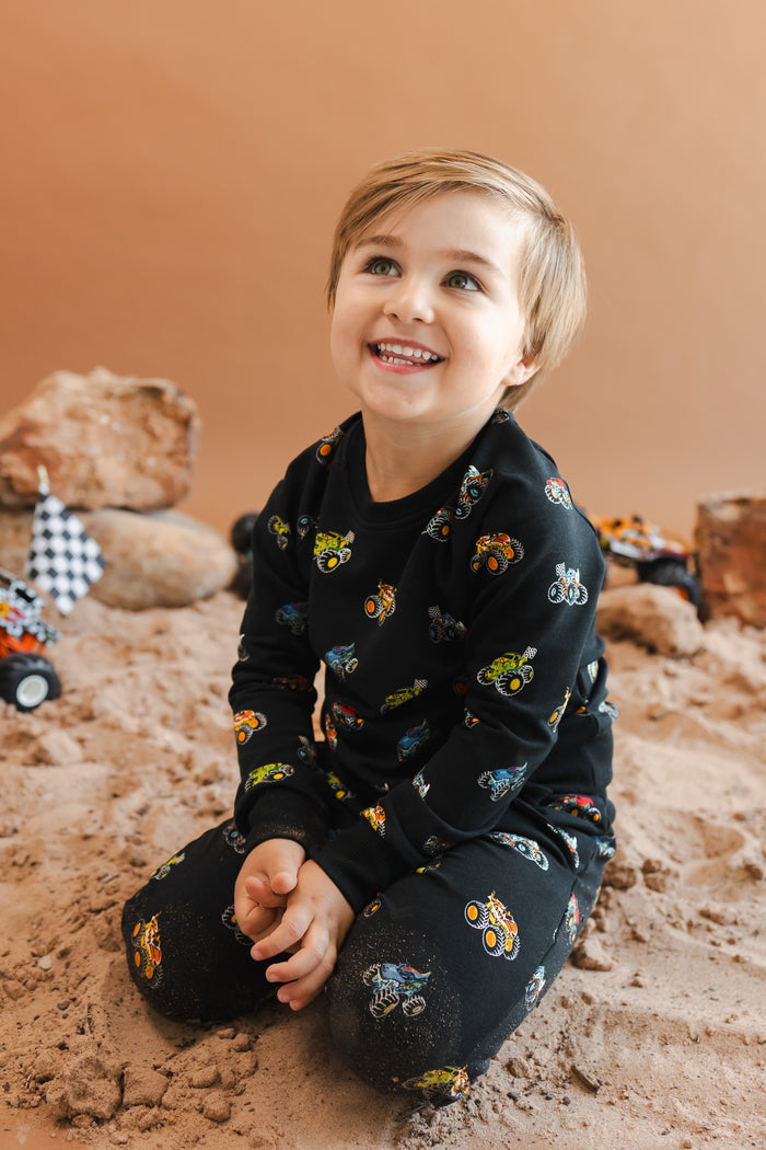 Boy sitting on sand in black Long Sleeve Jogger Set in Monster Truck print
