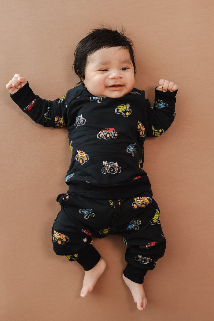 Baby wearing black Long Sleeve Jogger Set in Monster Truck print on beige background