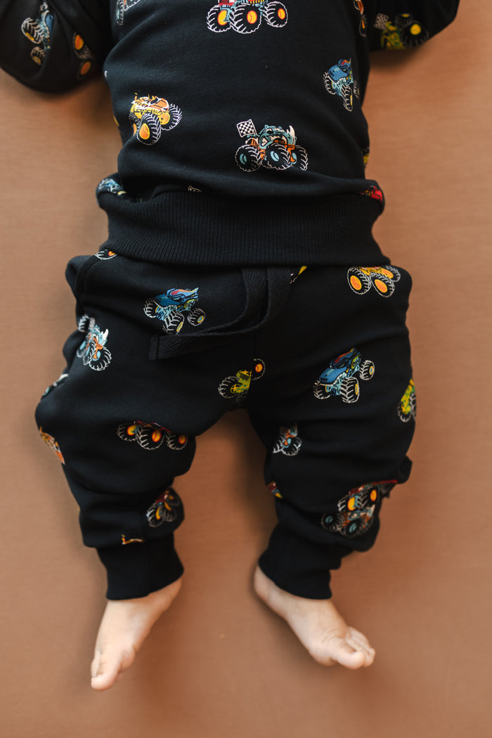 Baby wearing black Jogger pants in Monster Truck print on beige background