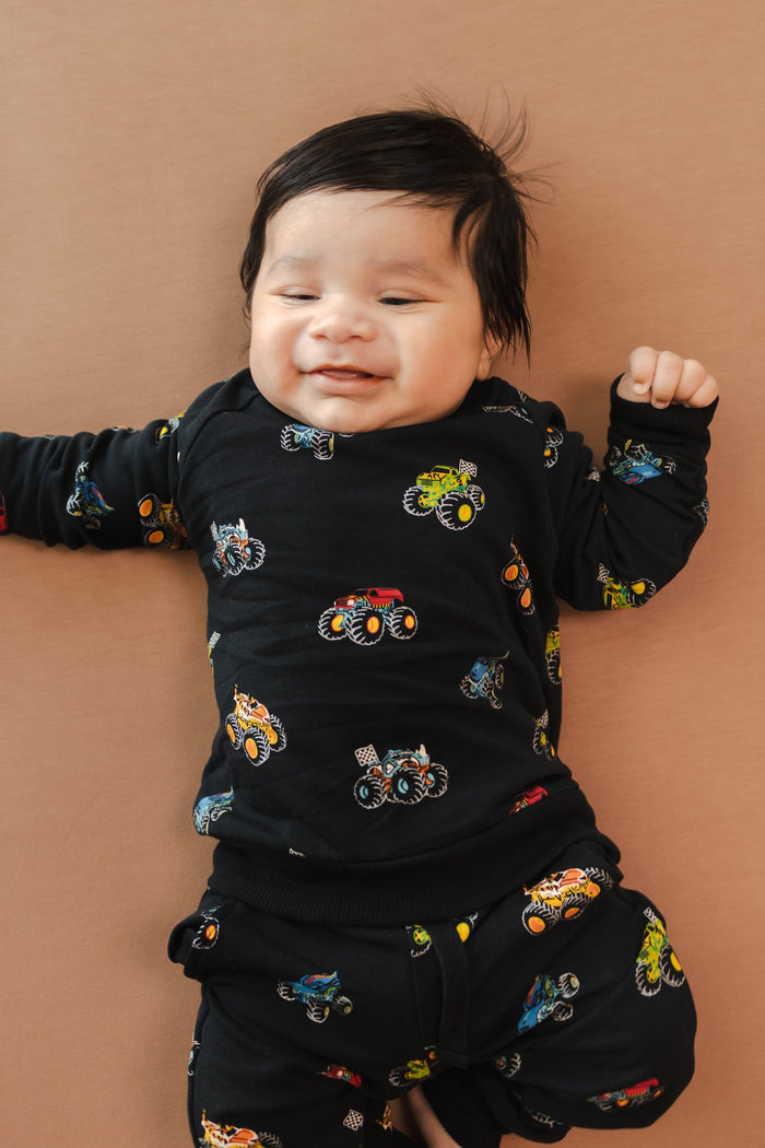 Baby wearing black Long Sleeve Jogger Set in Monster Truck print on beige background