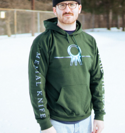 Forest green colored hoodie with the Hail The Sun logo across the chest in blue (circle with three lines coming out the bottom. On one sleeve, there is white text that says HAIL THE SUN, and on the other there is blue text that says MENTAL KNIFE. An individual is standing outside and modeling the hoodie with a fence and trees in the background.