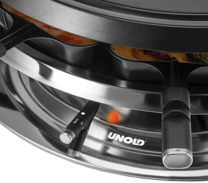 Nahaufnahme des Unold Raclette Multi 4 in 1 inklusive Raclette Buch mit einzelnen Pfännchen im Einsatz, leuchtender roter Anzeige und nach außen ragenden schwarzen Griffen.