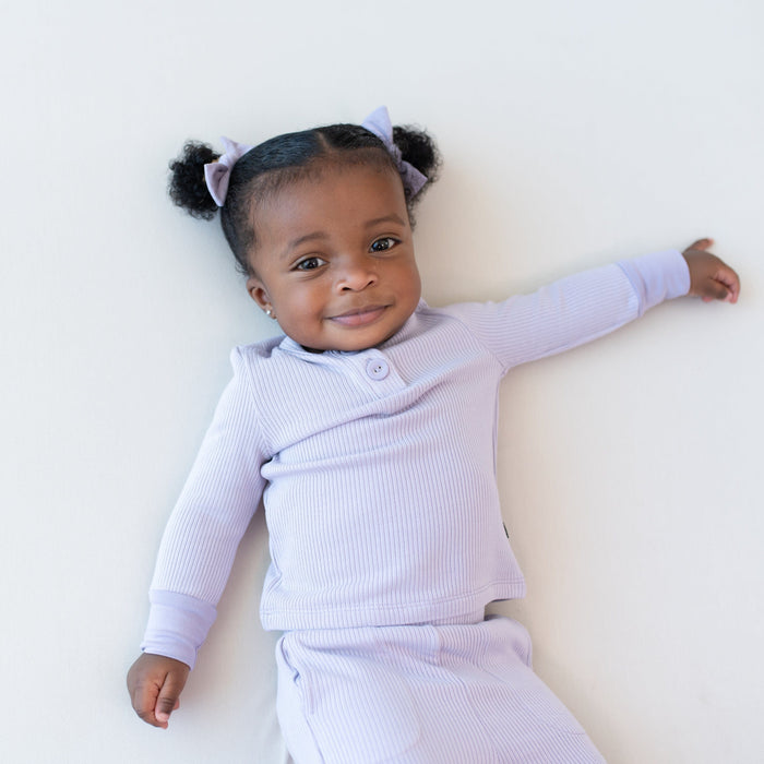 Child wearing Kyte Baby Bamboo Ribbed Infant Henley Set in Taro purple with matching Tiny Nylon Bows