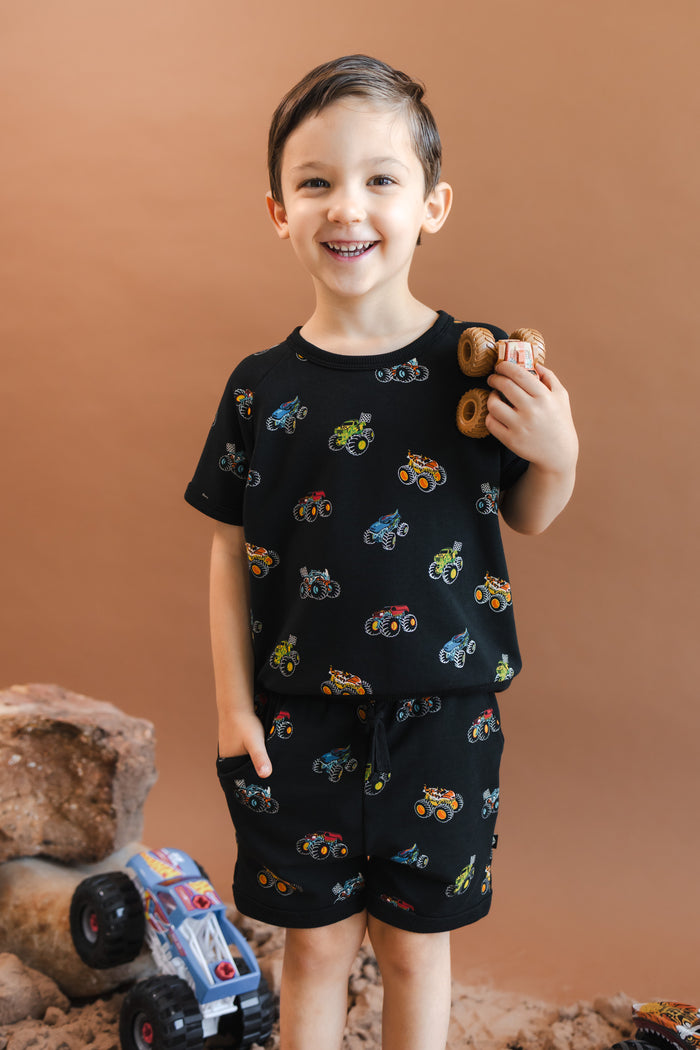 Boy wearing Black Short Sleeve Jogger Set in Monster Truck print holding toy truck on a beige background