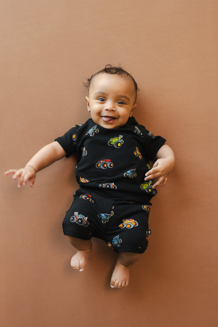 Baby wearing Black Short Sleeve Jogger Set in Monster Truck print on beige background