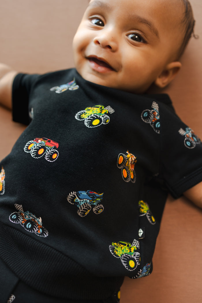 Baby wearing Black Short Sleeve shirt in Monster Truck print on beige background