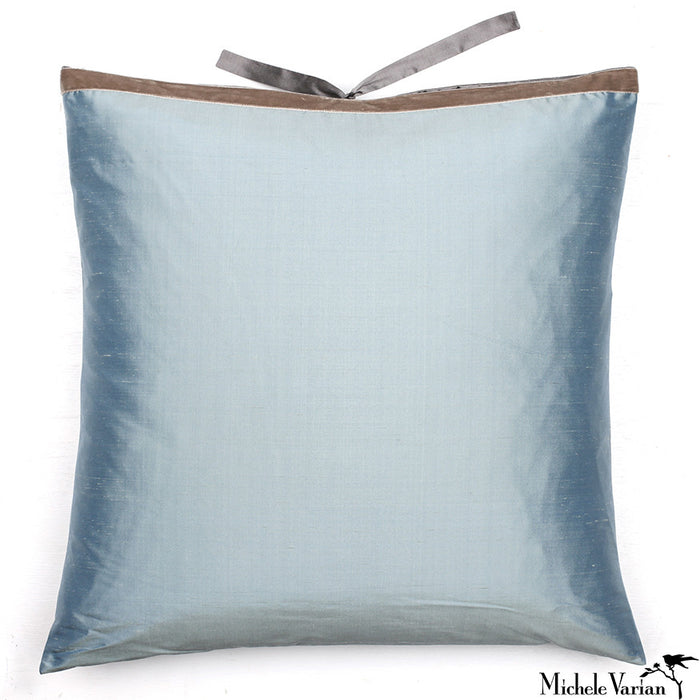 A square-shaped silk cushion in a light blue color with a solid velvet trim and a decorative silk tie at the top. Designed by Michele Varian and made in New York.