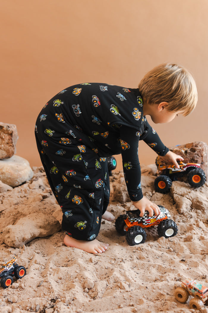 Boy playing with truck toys wearing a black Sleep Bag Walker with Monster Truck print on a sand