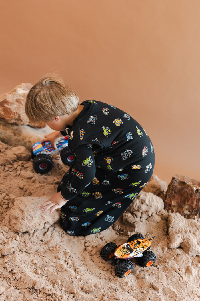 Boy wearing black Sleep Bag Walker with Monster Truck print playing with trucks on sand